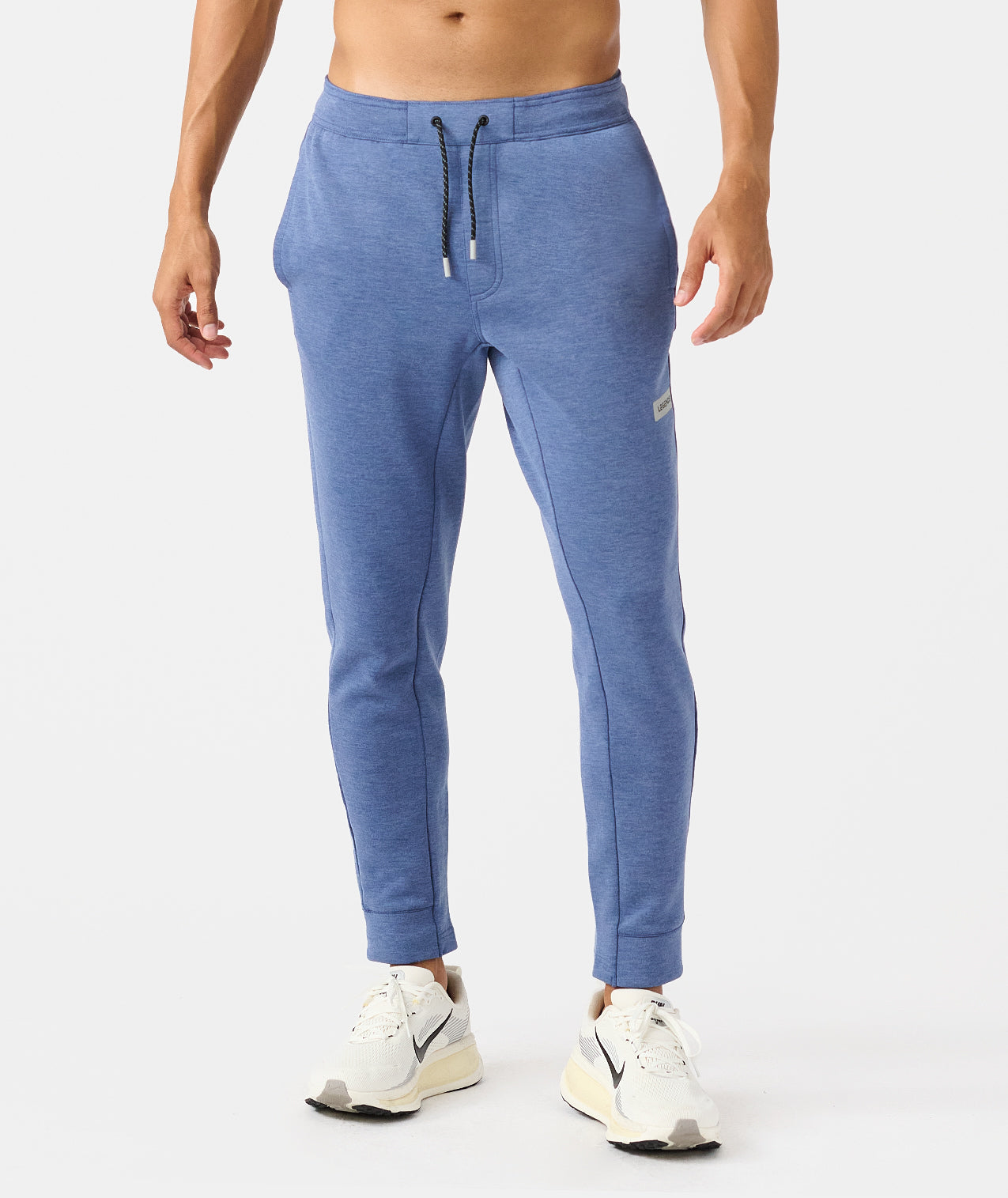 Man wearing heather blue joggers with drawstring waist and white sneakers. - 1