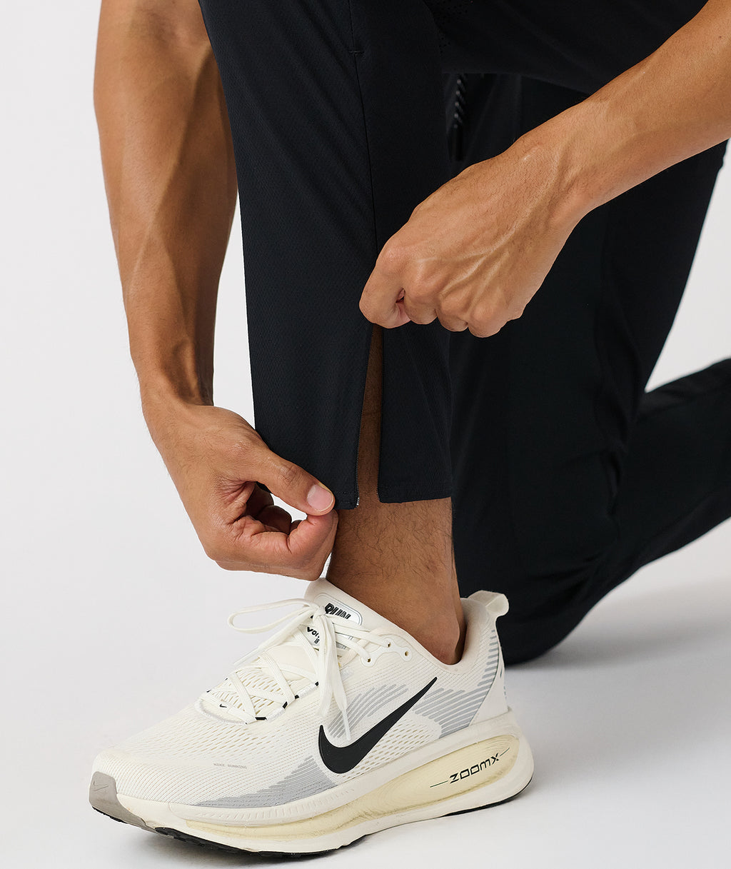 Black tapered pants with side seam detail shown on model wearing white sneakers. - 8