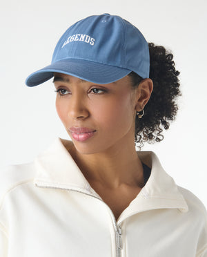 Blue baseball cap with white "Legends" text embroidered on front, worn by person with white zip-up jacket.
