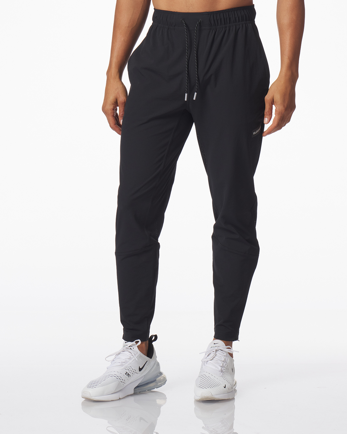 Black jogger pants with elastic waistband and drawstring, tapered leg, worn with white sneakers.